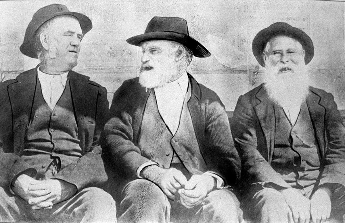 Black and white photograph of three elderly men in civilian clothing sitting in a row.