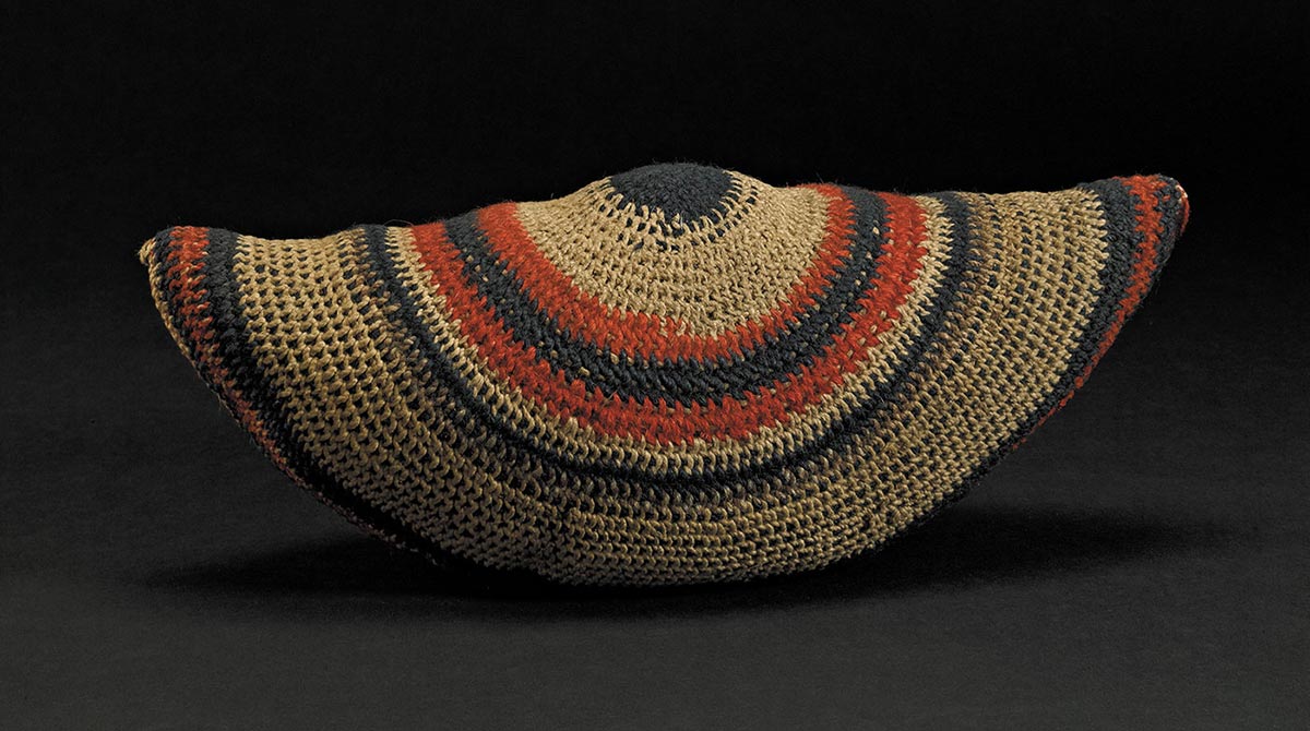 A semicircular shaped woven bag of wool and twine, with patterns of red and blue.