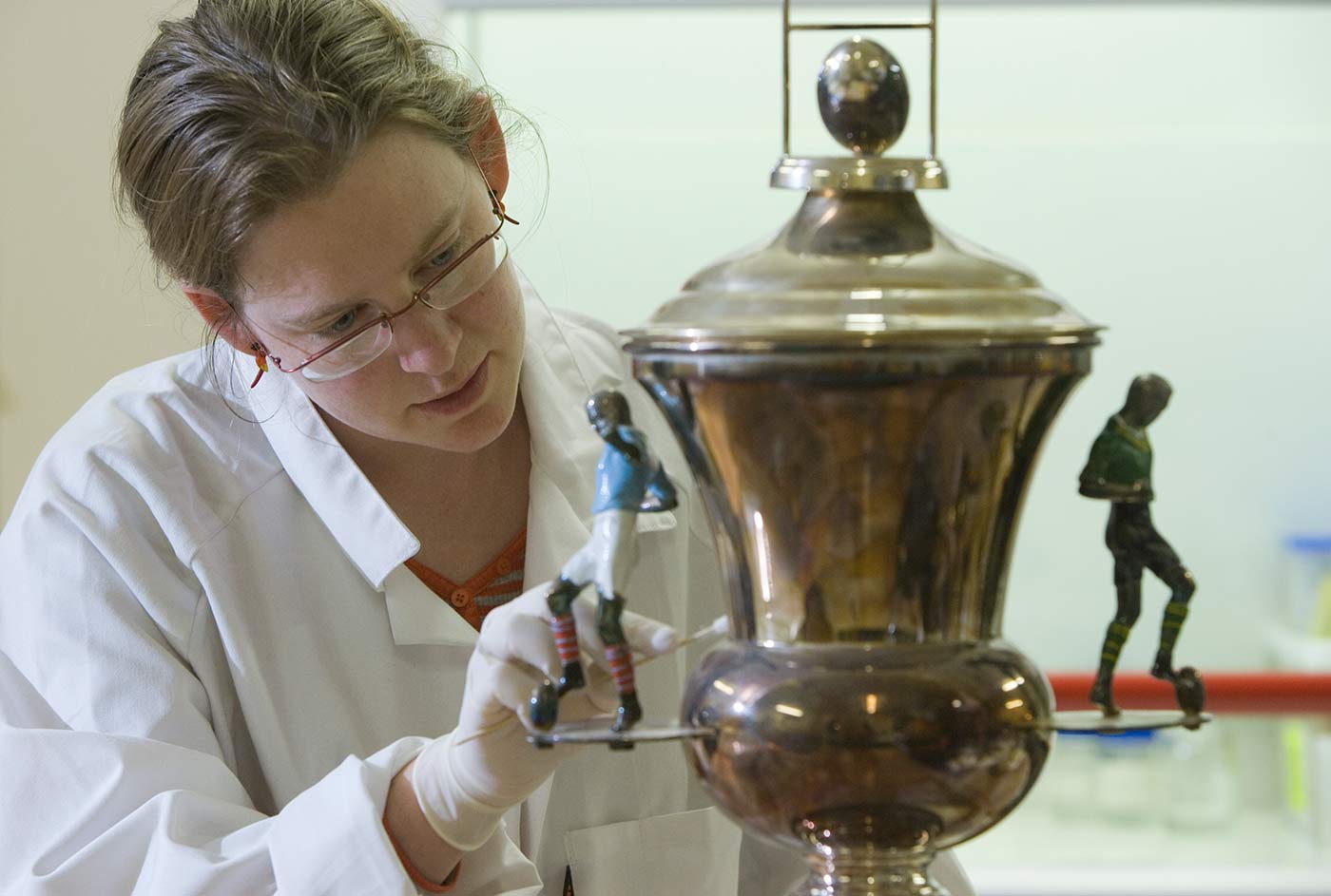 A woman wearing a white dust jacket works on a football trophy.