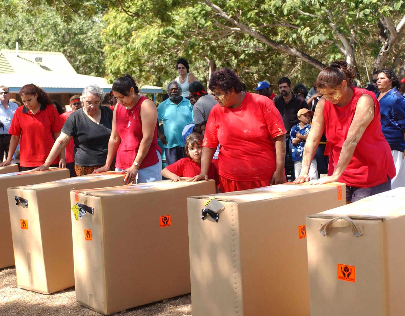 Photo of a large group of people standing around large cardboard boxes containing sacred material.