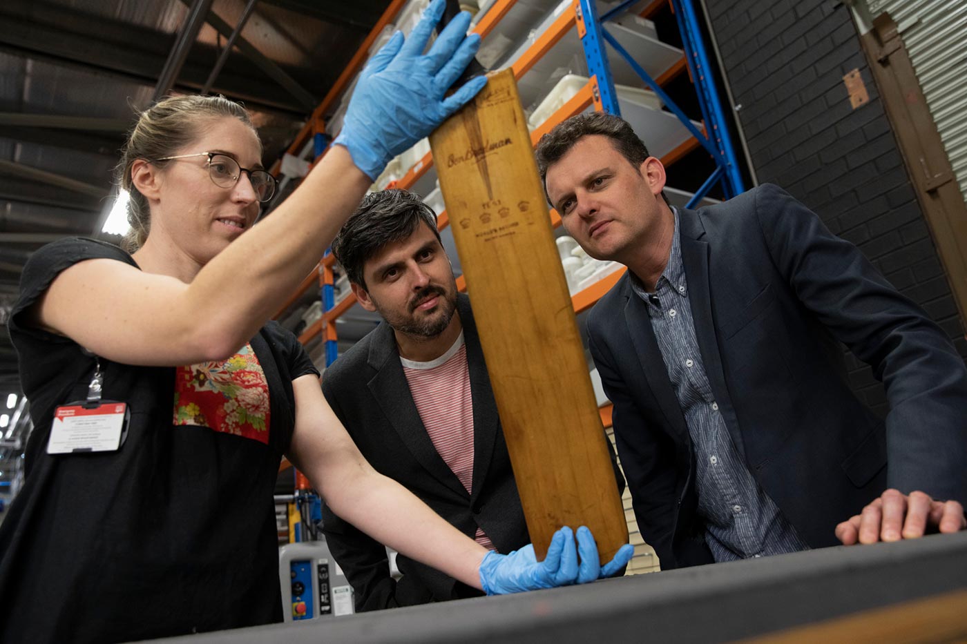 Slava and Leonard Grigoryan inspect a cricket bat that a female staff member is holding.