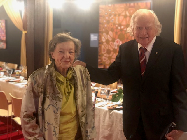 Picture of a woman and man in front of a long dining table.