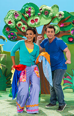 A woman and man dancing in front of a colourful cardboard tree.