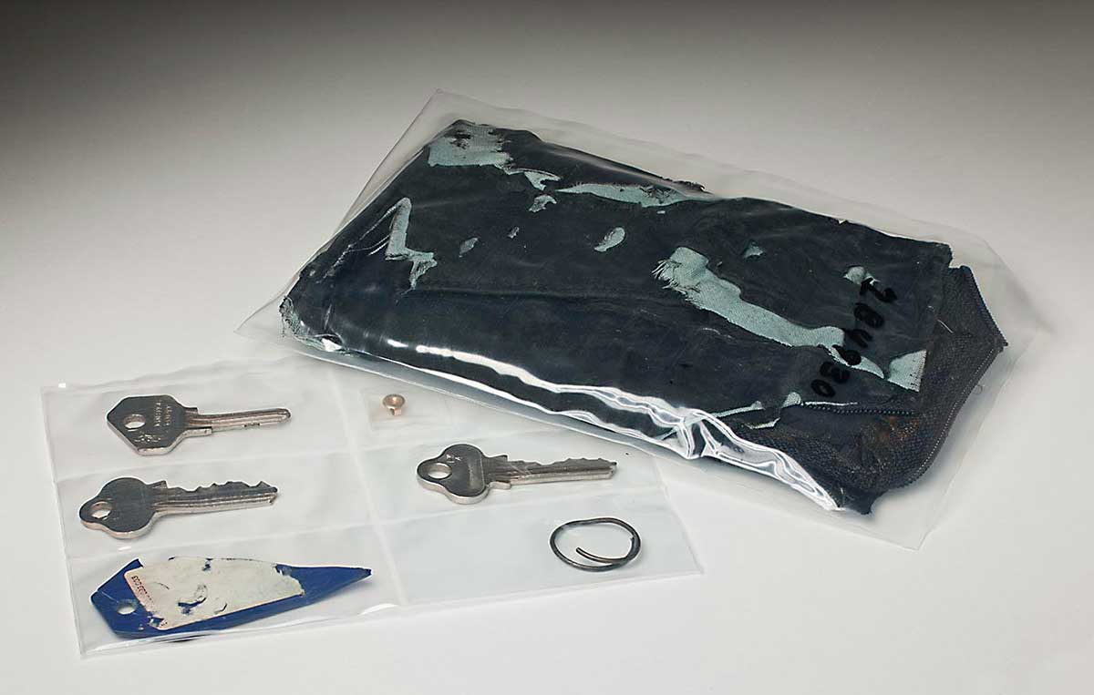 A dark blue leather wallet inside a plastic pouch, alongside another plastic pouch with six small compartments. These contain three silver keys, a remant of a blue plastic tag, a small metal ring and a metal earring fixture.