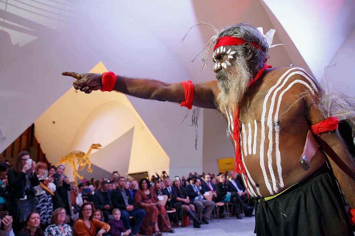 Man with body paint pointing while an audience watches.