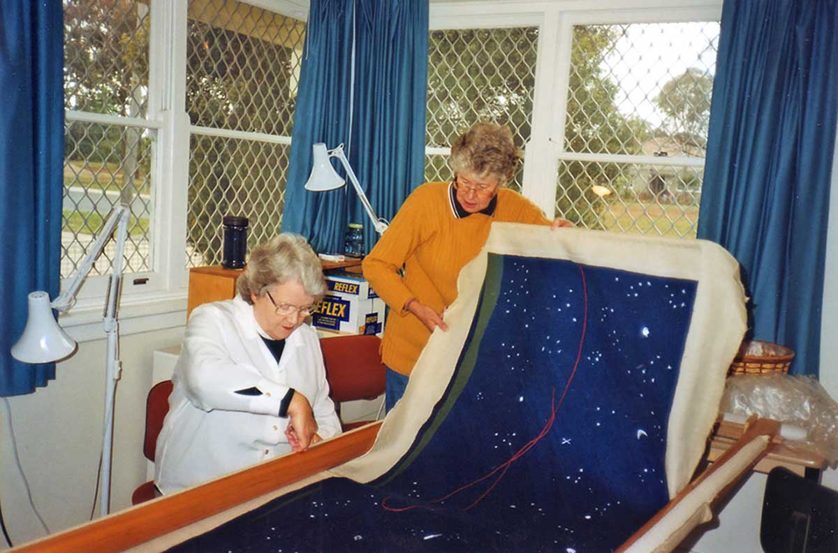An indoor photograph of two people holding and examining a long piece of artwork.
