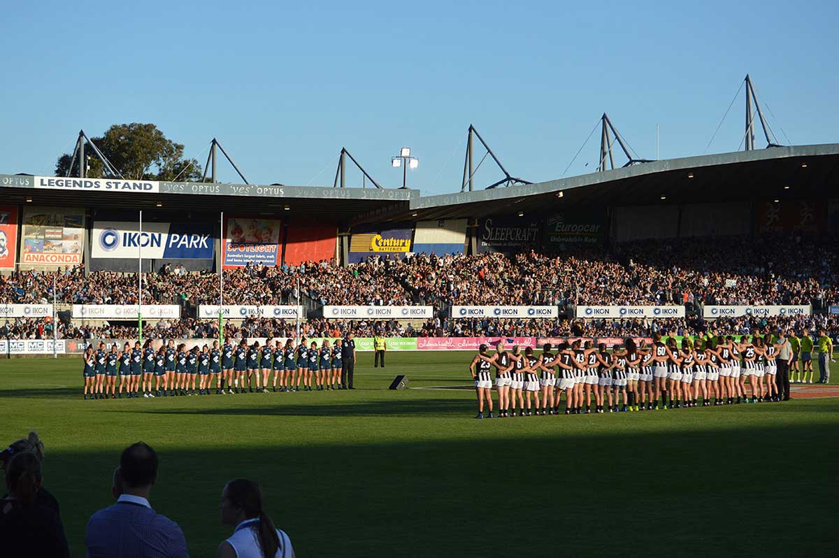 A stadium filled with football supporters seated in the stands and players lined up on the field.