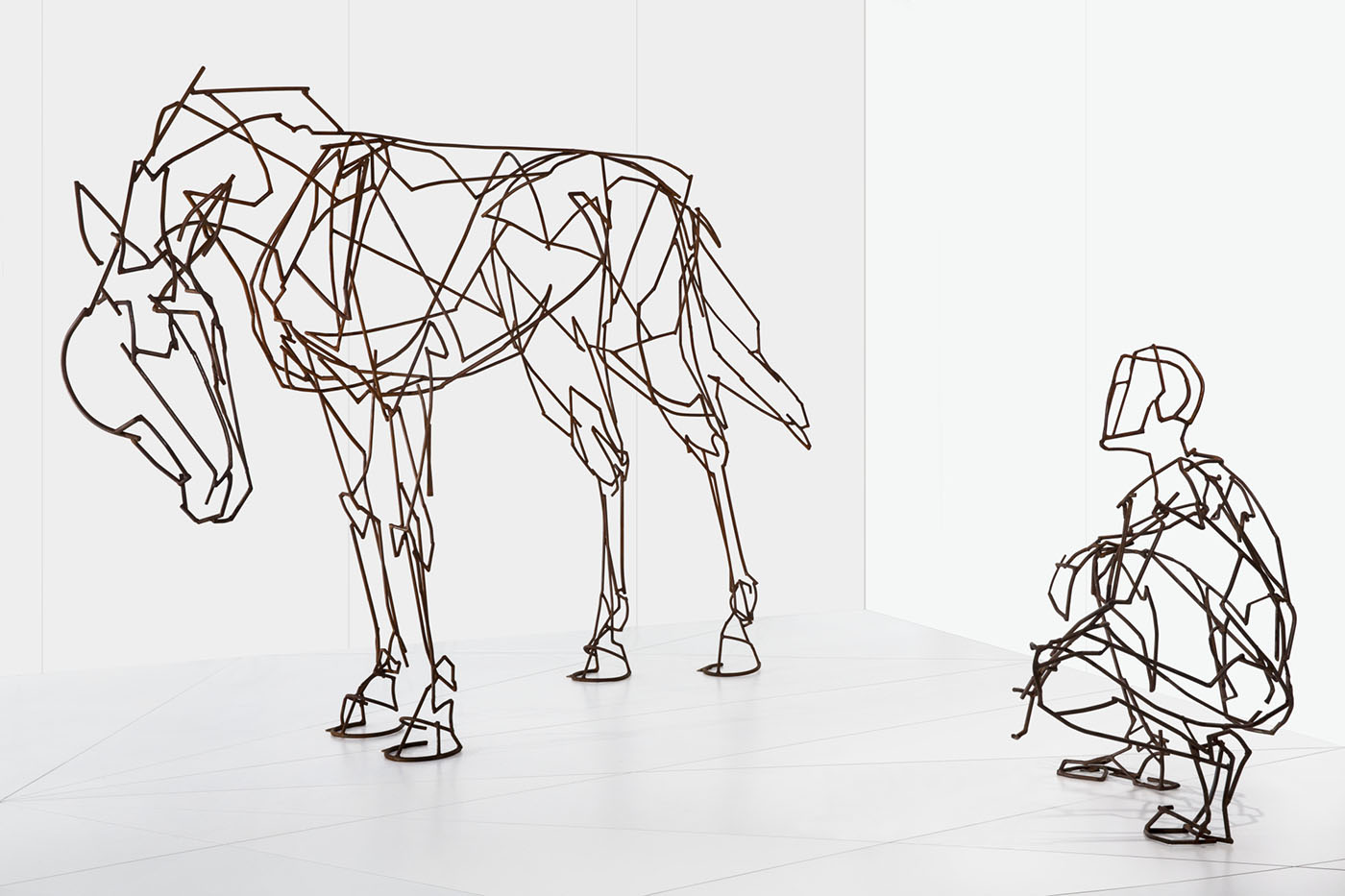 Metal sculpture showing a person squatting away and to the side of the form of a horse.