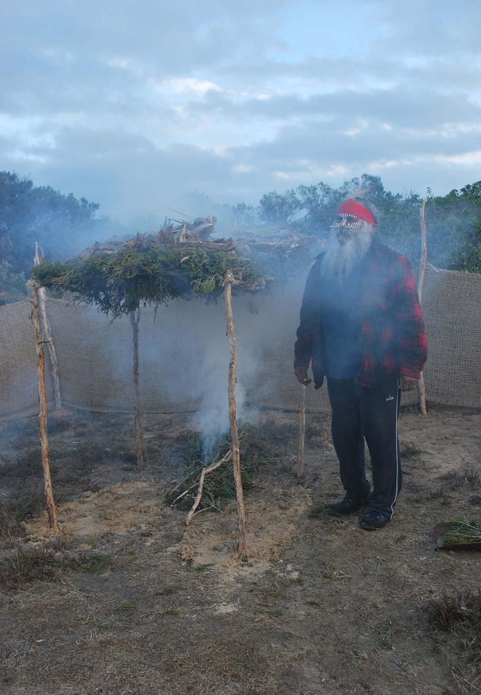 Photo of a man with face paint and bandana taking part in a smoking ritual.