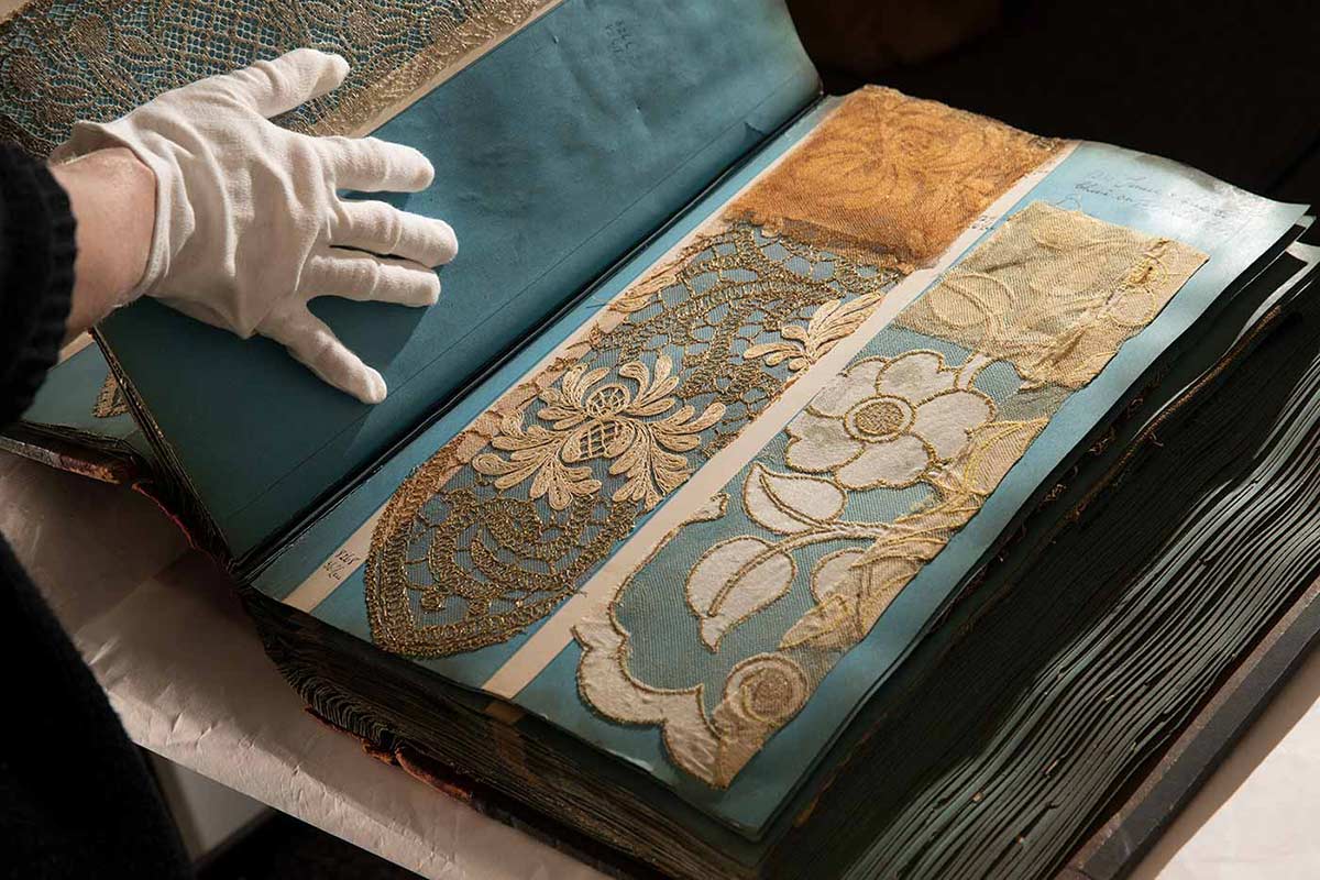 Colour photograph of a gloved hand flipping through lace samples in an large sample book.