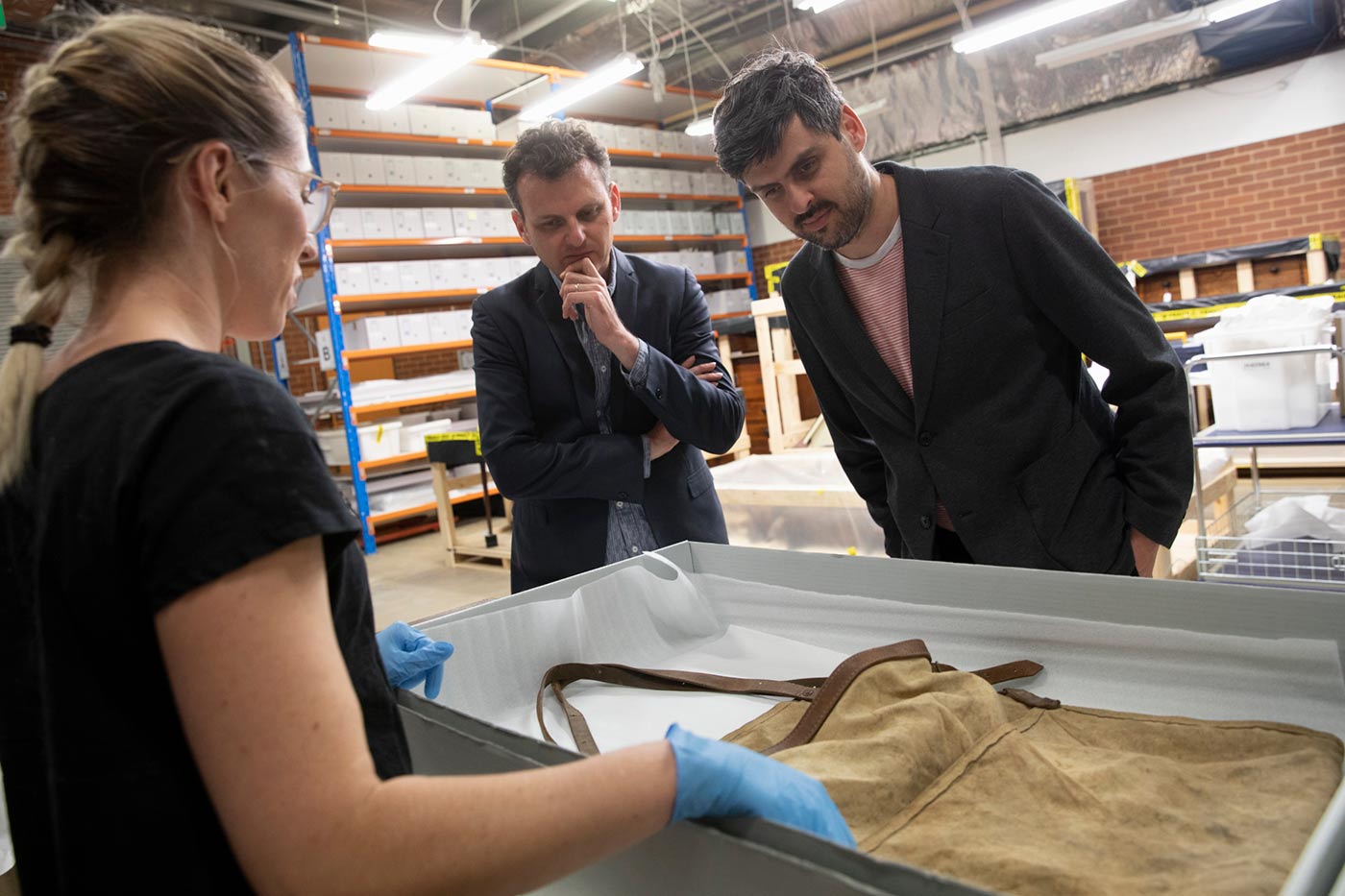 Slava and Leonard Grigoryan inspect an old apron displayed in a conservation box that is presented by a female staff member.
