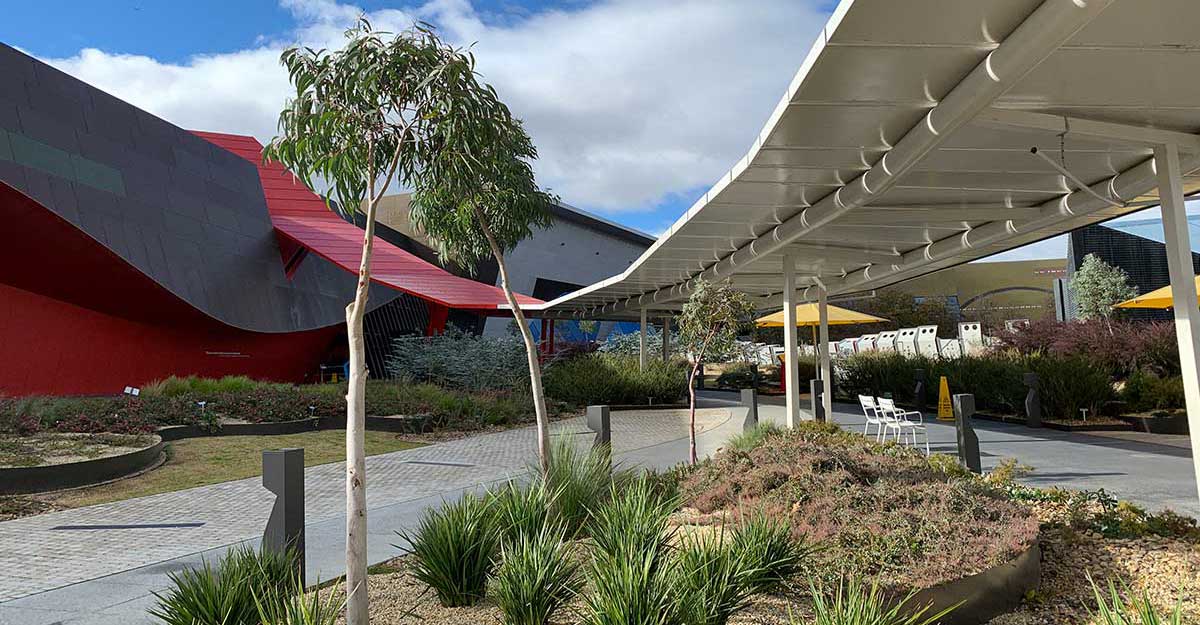 Landscaped gardens and paved walkways leading up to a modern building with sculptural architectural features.