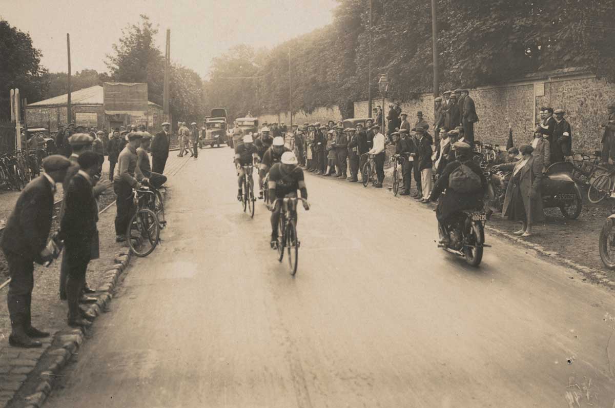 A black and white photo of Hubert Opperman leading a four-man team through a village during the Tour de France, 1928.