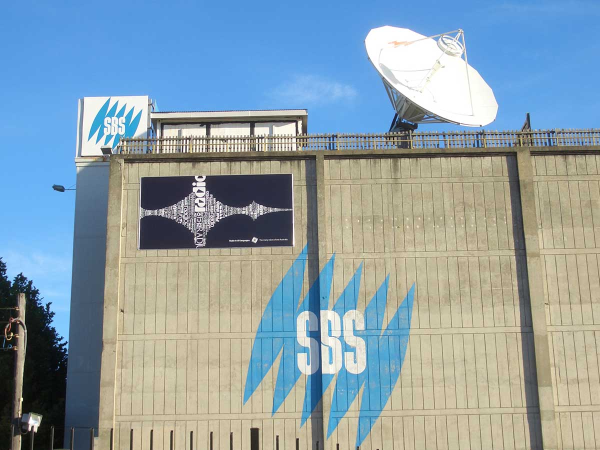 The outside of a large building which has a large white satellite dish and SBS logos on the side of the building.