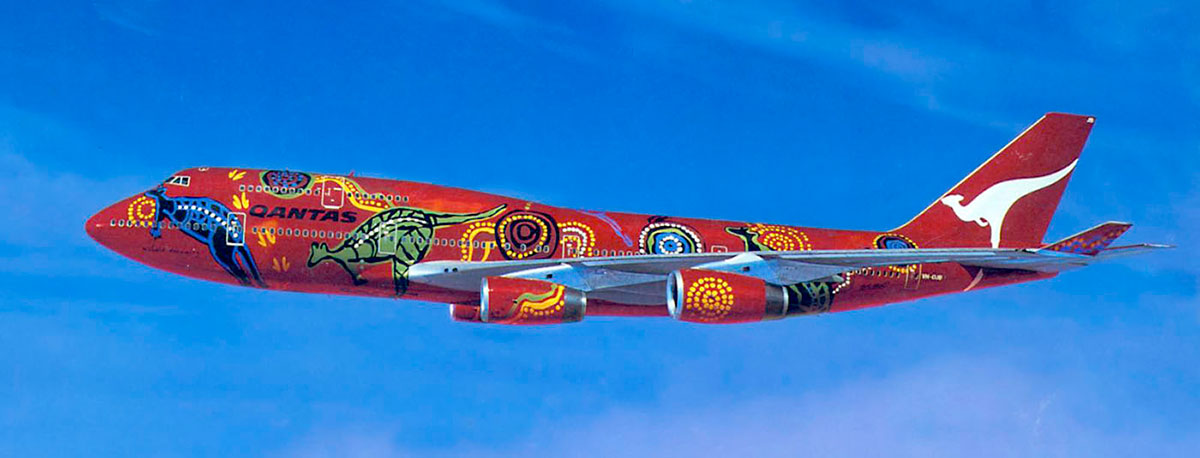 Side view of a large plane with Aboriginal designs painted on a red background.