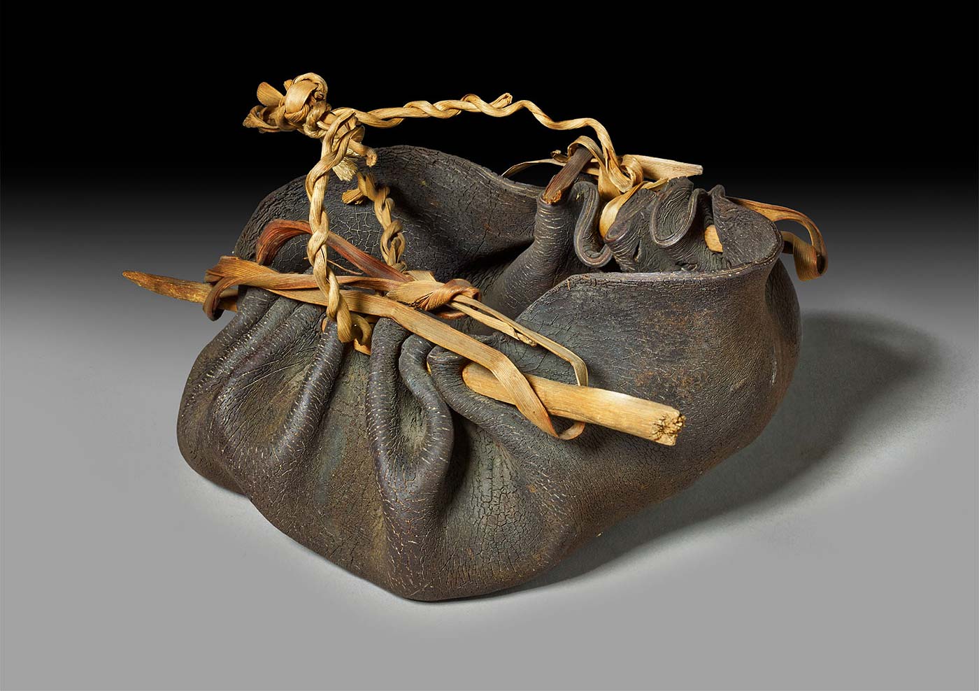 A piece of kelp pierced by two sticks and shaped to form a rounded container with a fibrous handle.