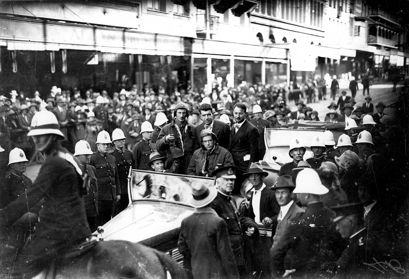 The crew of the Southern Cross in a car surrounded by people and policemen