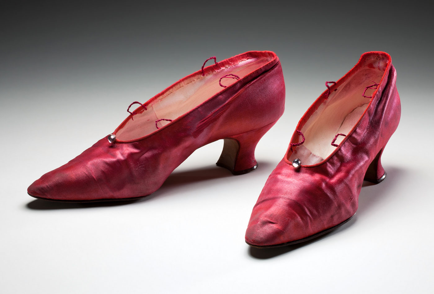 A pair of pink-dyed satin shoes, with a clear bead at cenre top, a Louis heel, narrow pointed toe and two thread loops on each side of the foot opening, for ankle ties.