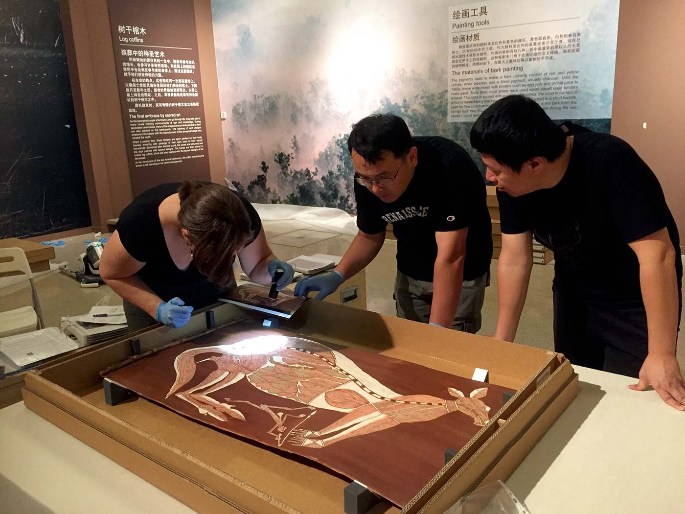 Three museum staff inspect an artwork featuring a kangaroo.
