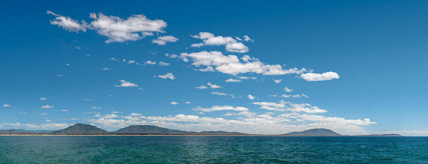 Colour photo of a bay with a beach and mountains in the background.