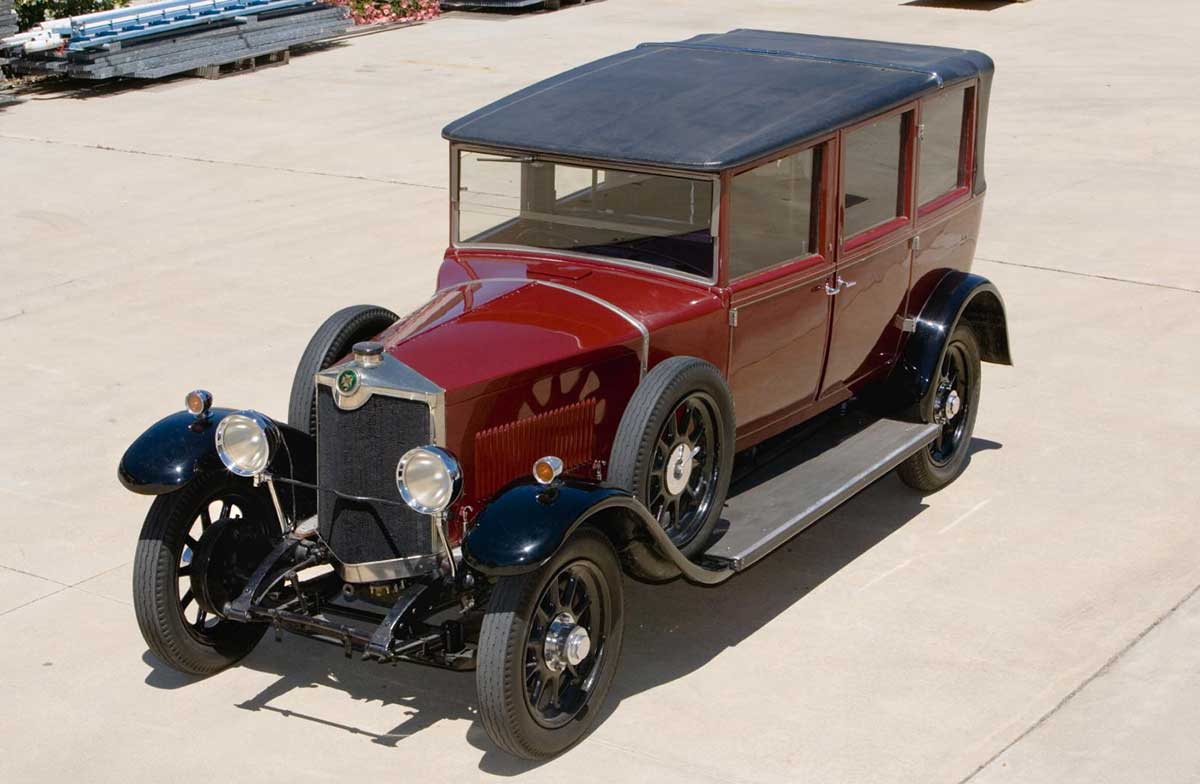Elevated view of a polished maroon vehicle, with black trim and black leather roof. The car has running boards and mudguards.