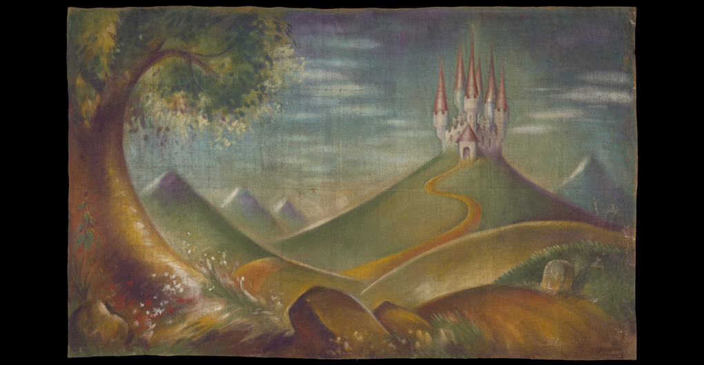 Large hessian backdrop depicting a castle in the background with six spires and a tower. The castle is surrounded by mountains and sits against a blue, purple and green sky. In the foreground are rolling hills, a tree, flowers, rocks and a route marker. 