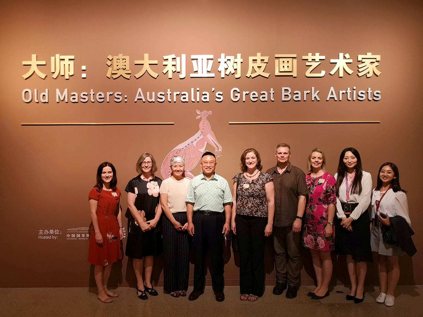 A group of people in front of a gallery wall with the title 'Old Masters: Australia's Great Bark Artists' beneath its Chinese translation.
