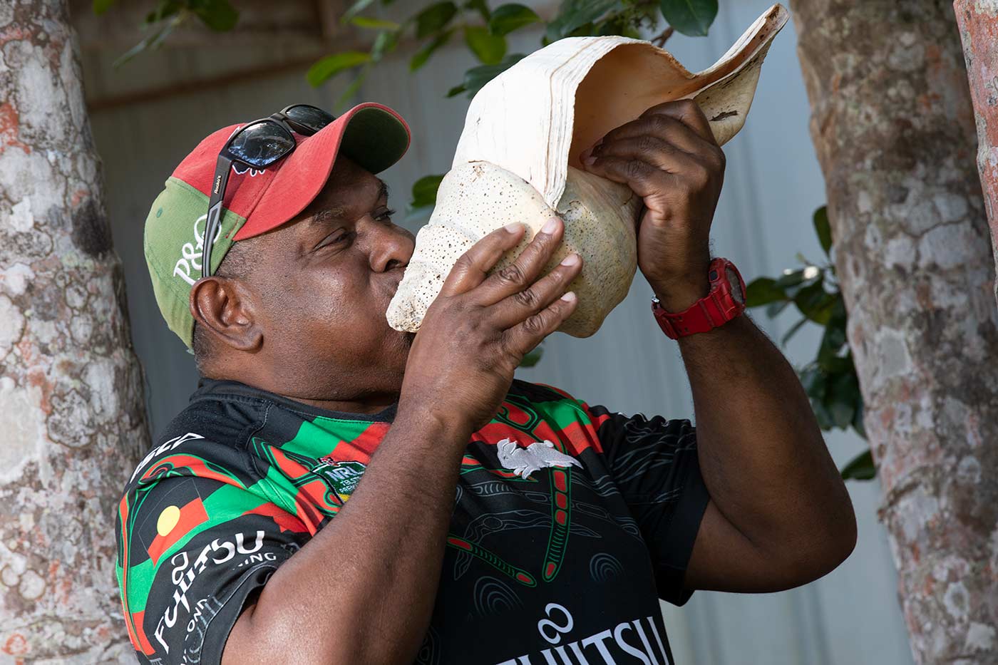 Colour photo of a man blowing into a large conical shell.