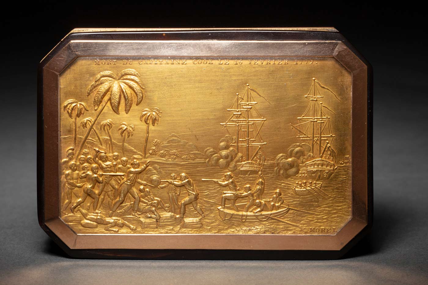 Tortoiseshell snuff box, incorporating a gold plaque on the lid that shows the death of Captain Cook at Kealukakua Bay in 1779, with boats on the harbour in the background. Relief text across the top of the gold plaque reads 'MORT DU CAPITAINE COOK LE 16 FEVRIER 1779'. The artist's signature 'Morel' appears at the bottom right corner.