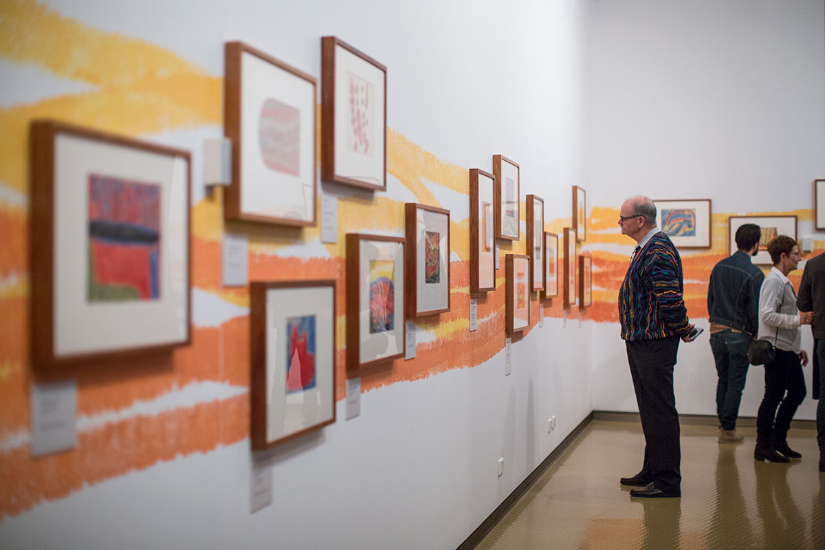 Visitors viewing a series of framed works on a gallery wall.