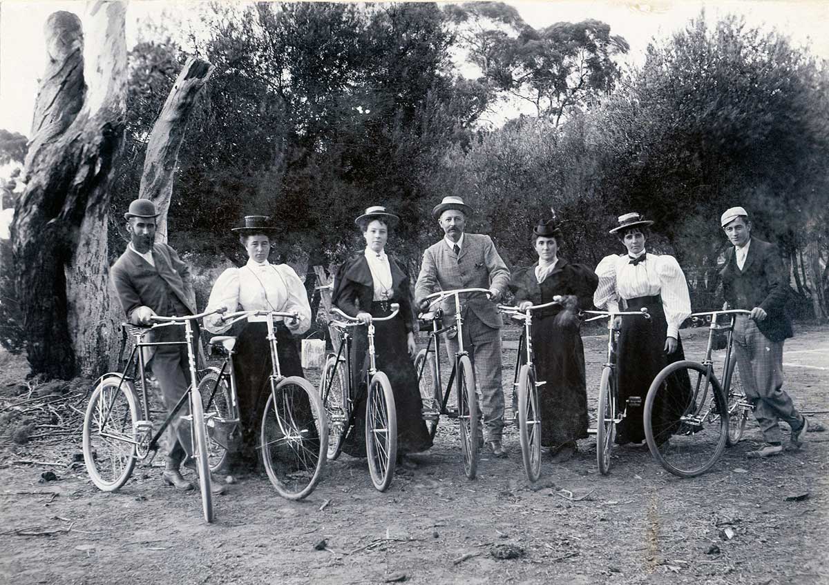 A black and white photo of a group of men and women standing with their bicycles.