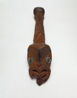 Architectural ornament A canoe ornament made of wood and coloured red. The carving features a human face with tongue extended and the larger face with inlaid mother-of -pearl eyes.