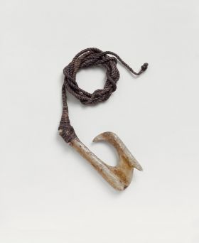 Fishhook makau Fishhook made of bone with a straight shank. A barb is located on the outer side of hook, directly below the point. A brown fishing line is attached to the hook.