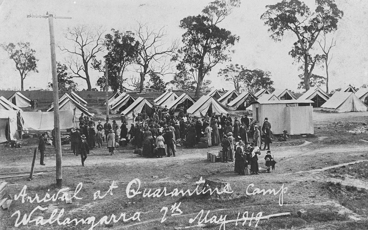Black and white photograph of a crowd of people amongst tents set up in bushland. Hand written text reads: