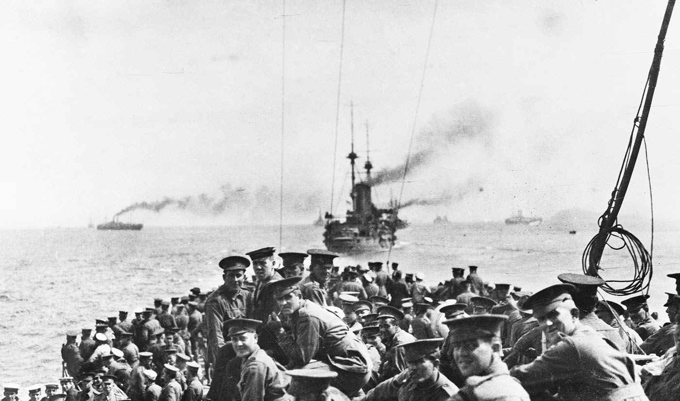 Grainy black and white photo taken on board a boat full of Australian soldiers, with ships in background.