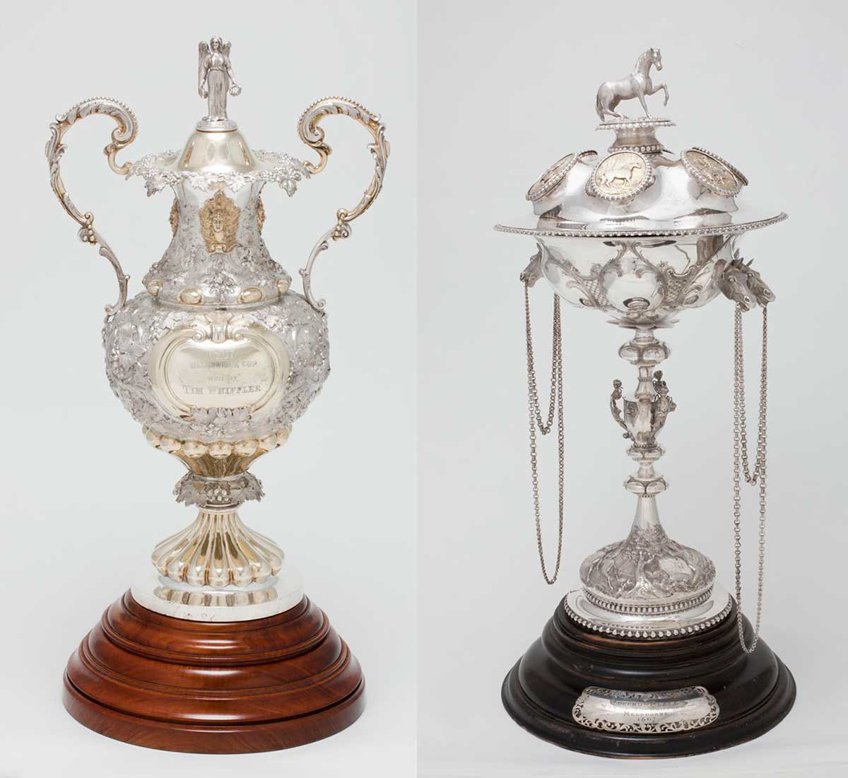 The Melbourne Cup trophy is mostly silver with two ornate handles and mounted on a wooden base. The Queen's Plate trophy has a horse on the topy standing a rounded silver globe mounted on a long stem. Chains are draped from the globe.