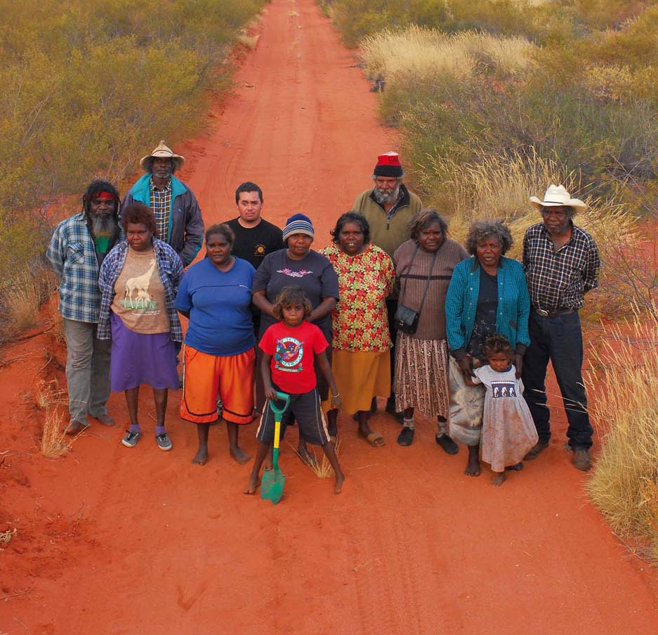 Group portrait of people standing on a red sand track.
