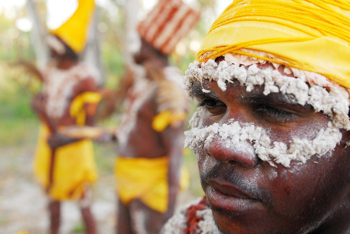Colour photograph of a close up of a young man in costume with two other people wearing the same attire in the background.
