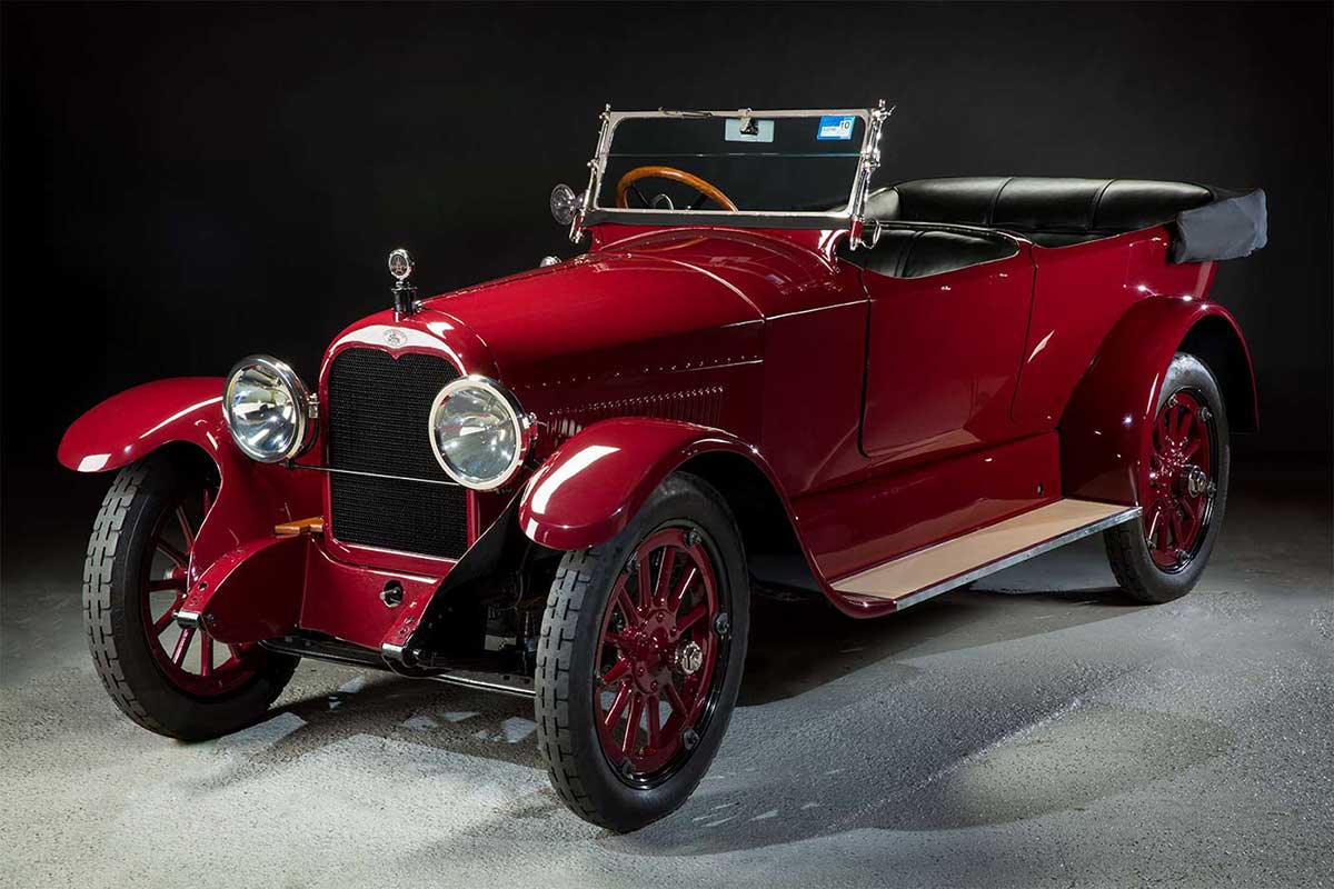 Side view of a polished red open-topped motor car with running board and elongated mudguards.