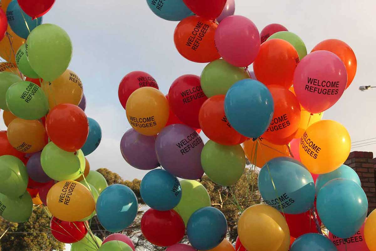 Multicoloured balloons with 'Welcome Refugees' on them flying in the air.