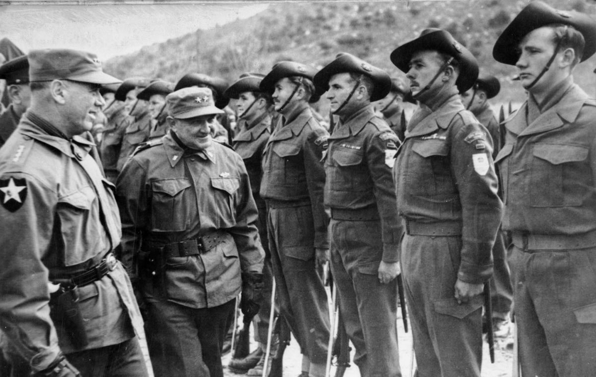 A short, smiling man in his fifties or sixties in Army uniform inspects Australian soldiers standing at attention.