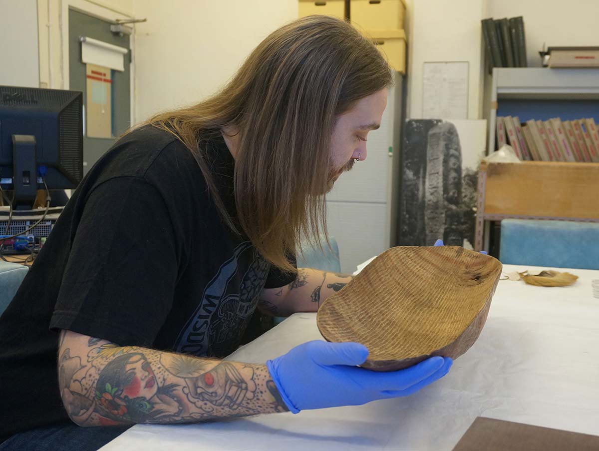 Tynan Waring at the British Museum with a painted bowl made of wood.