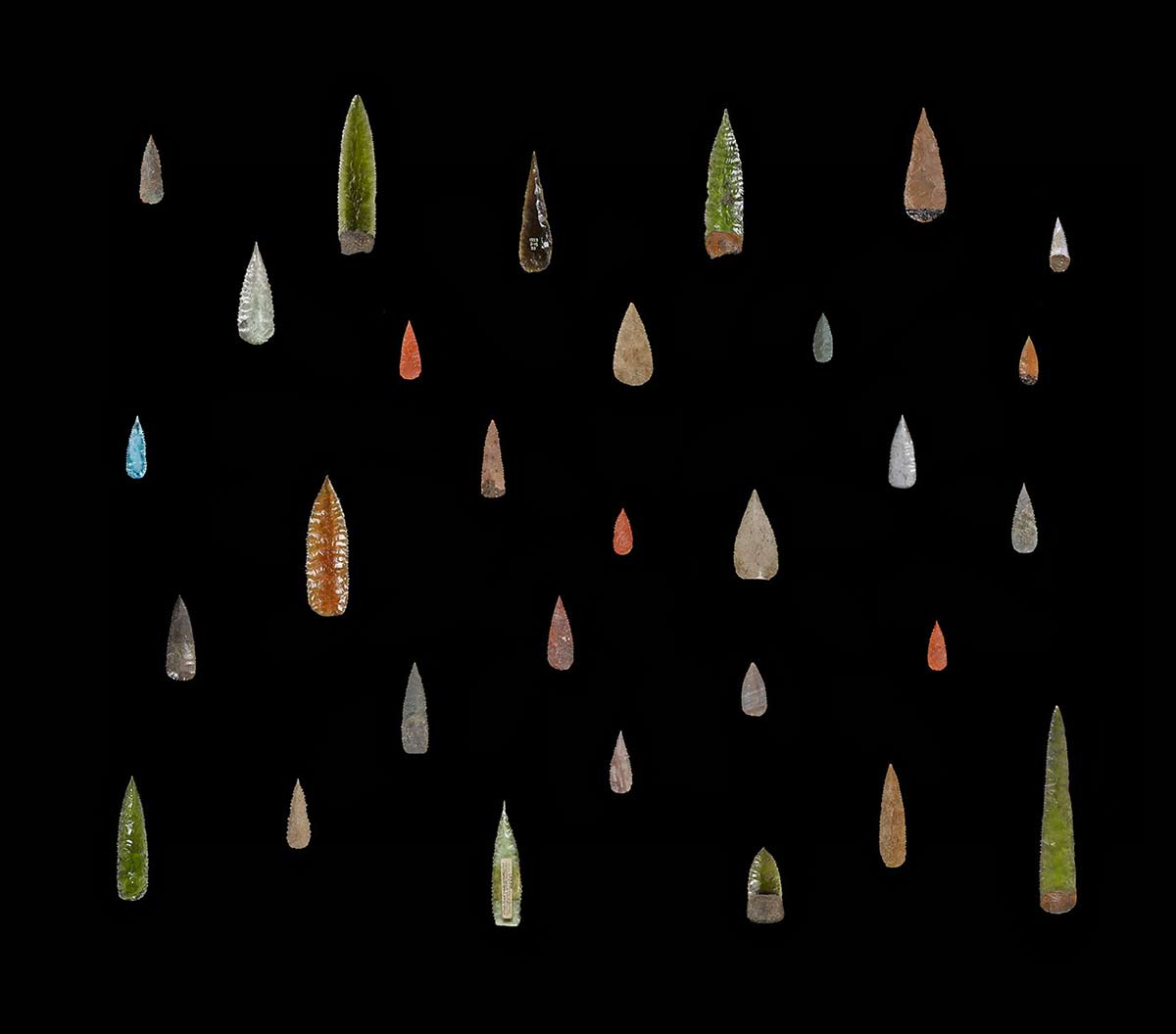 A collection of spearheads made from various materials including glass.
