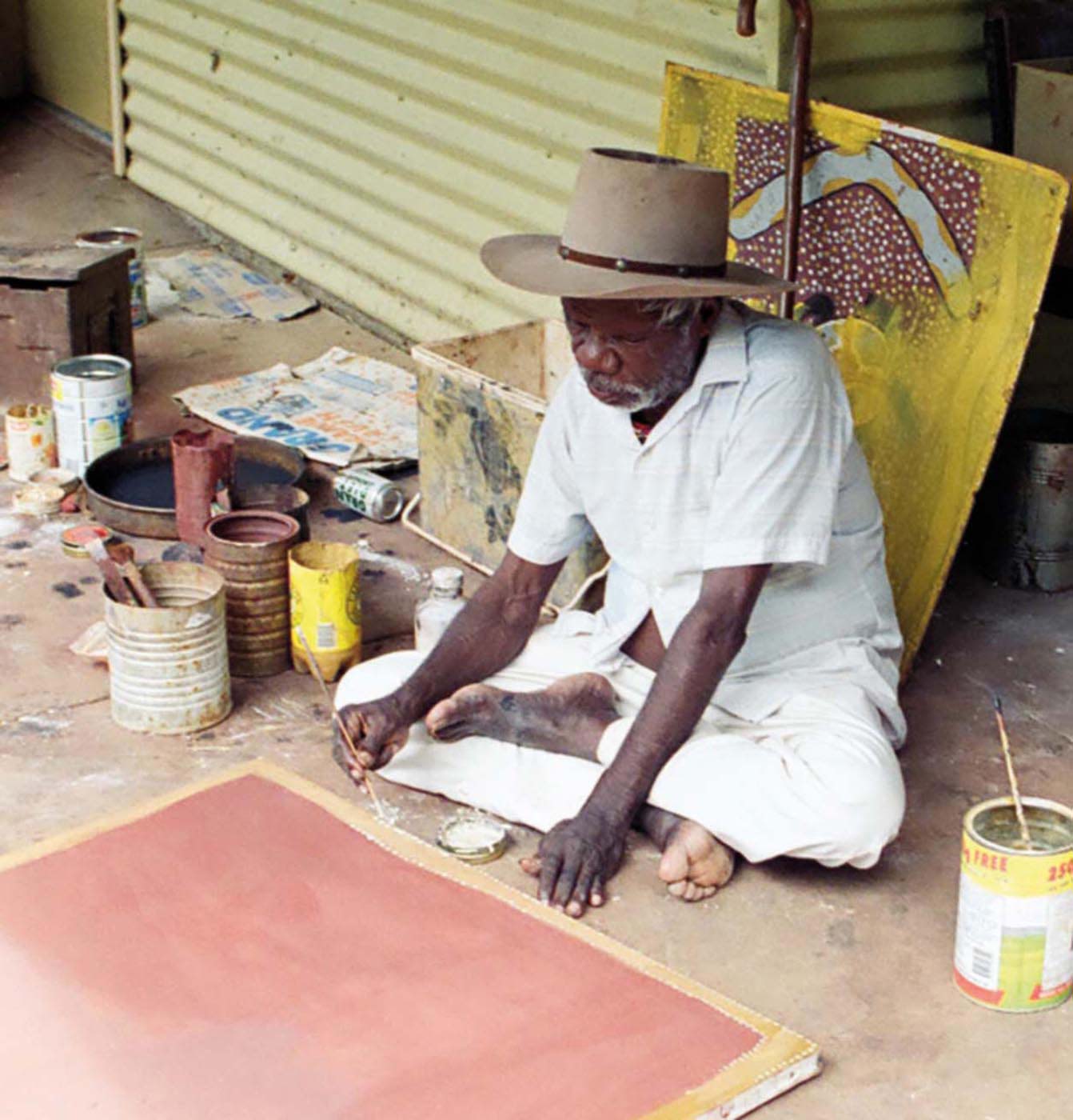 Colour photograph of a man sitting on the ground and painting.