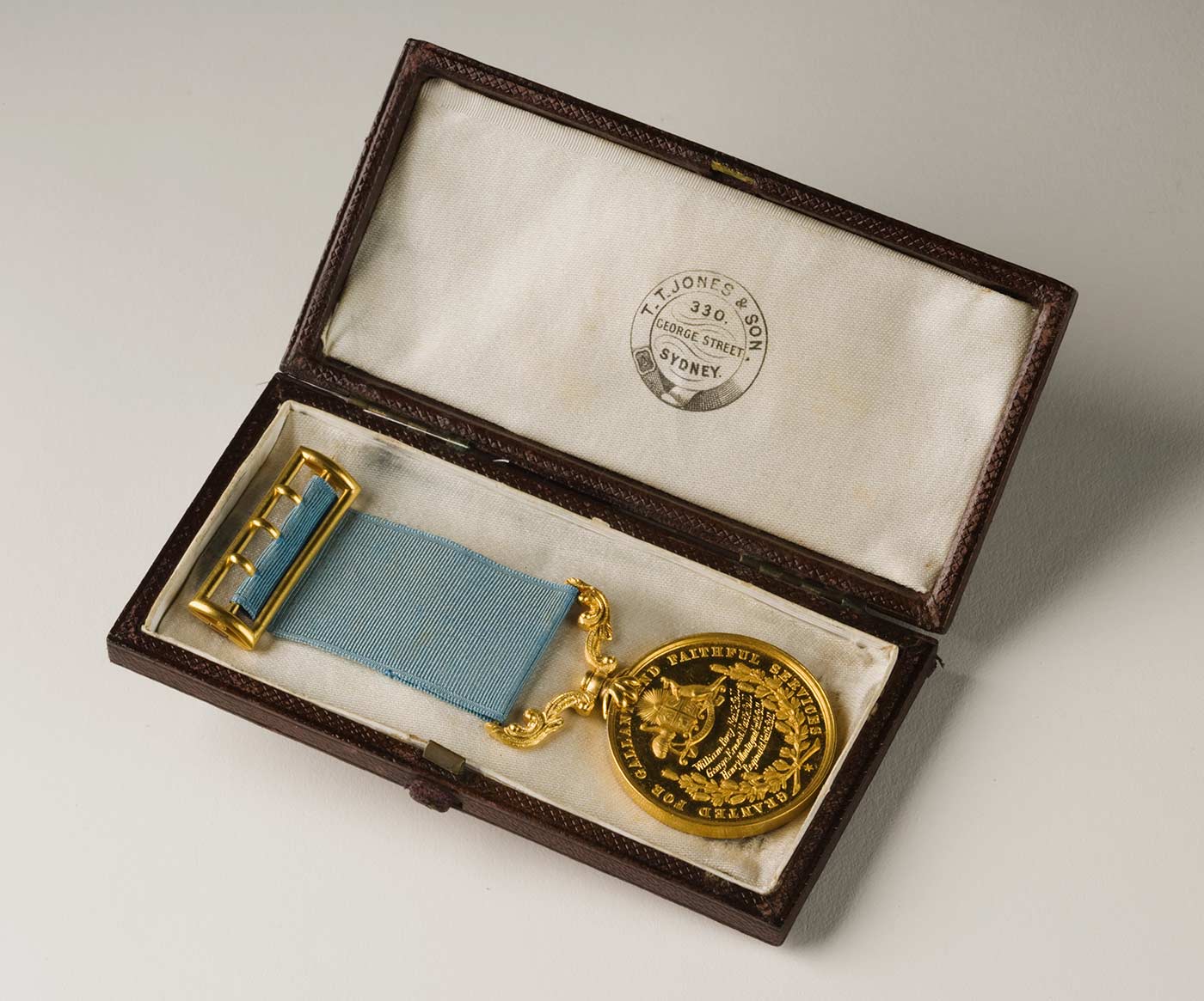 Bushranging medal with words in capitals around the edges 'GRANTED FOR GALLANT AND FAITHFUL SERVICES' with light blue ribbon and gold clap displayed in its box with makers stamp on inside of lid.