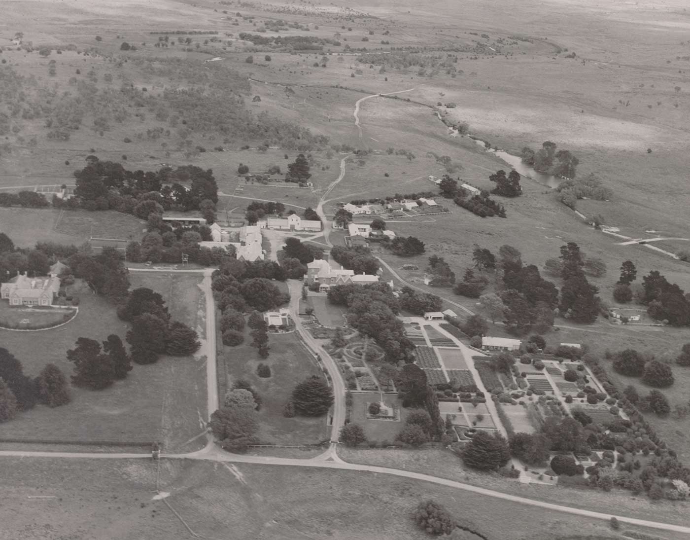 Black and white aerial photo of Springfield, showing several large buildings at centre, with formal gardens in the foreground and a small watercourse and paddocks behind.