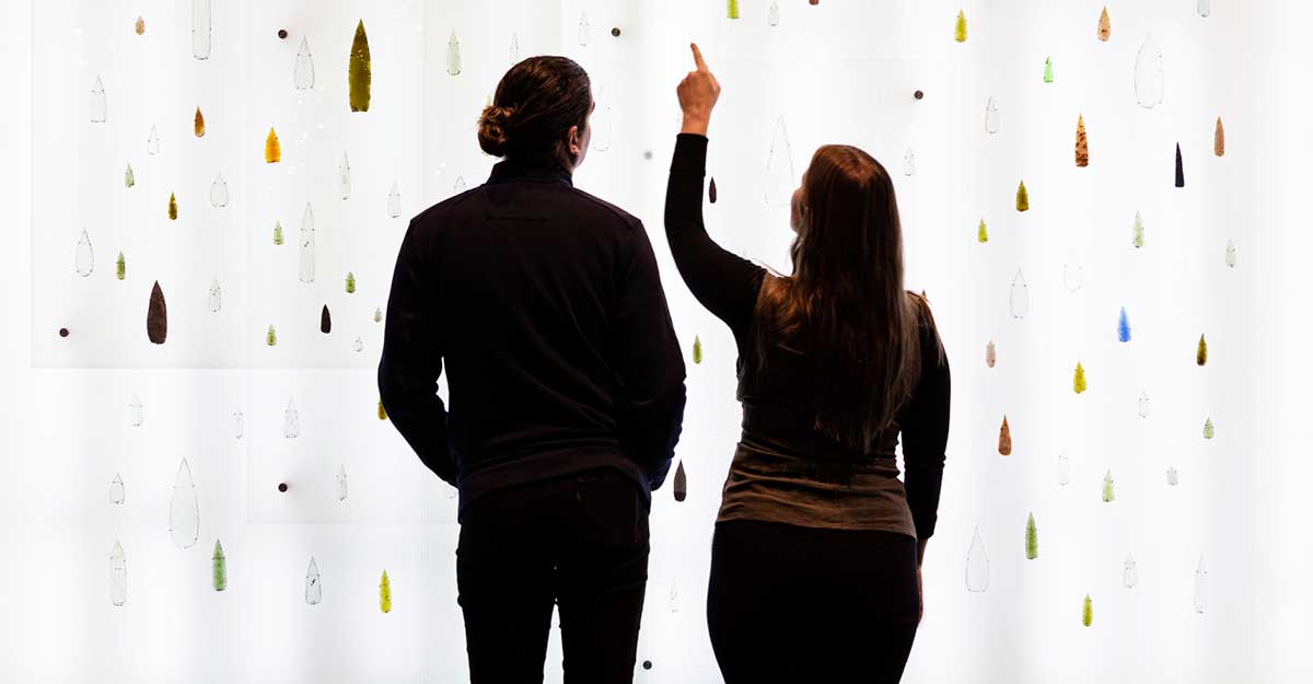 Two visitors standing in front of a large digital screen.