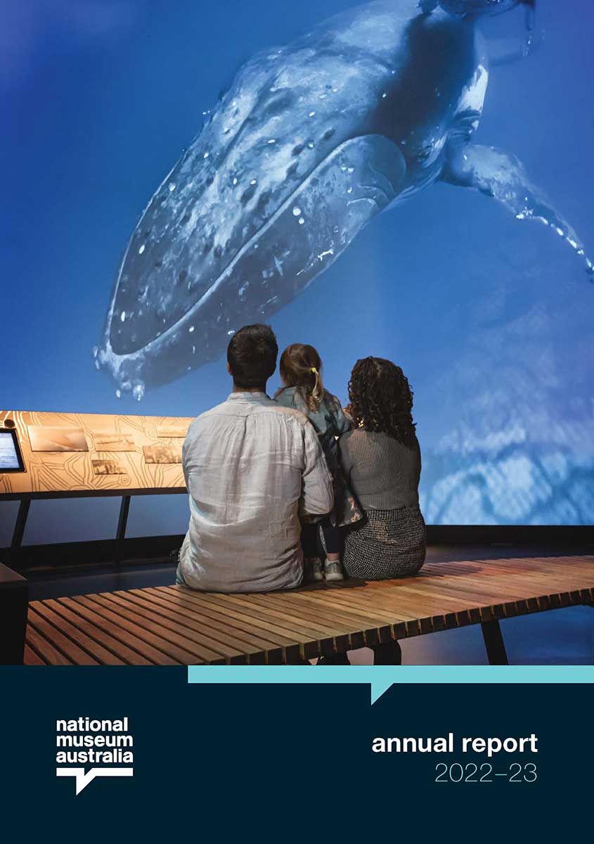 Cover of the National Museum of Australia 2022 to 2023 Annual Report. The cover features a photo of a man, woman and child sitting in front of a large digital screen of an underwater scene with a humpback whale.