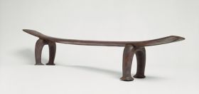 Headrest kali Headrest made of wood, the ‘seat’ is slightly curved and supported by a pair of horseshoe-shaped legs. The ‘seat’ becomes wider from the middle towards both ends.