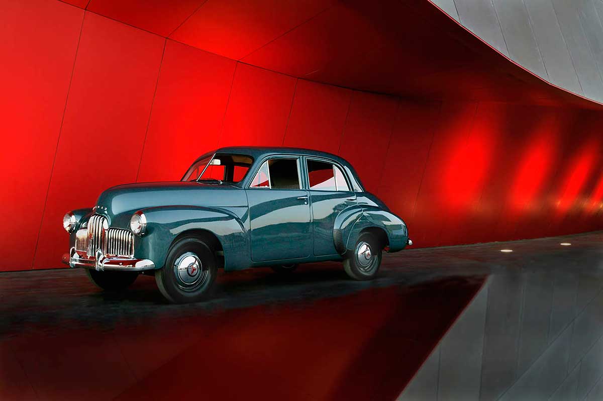 A blue motor sedan outside a red building.